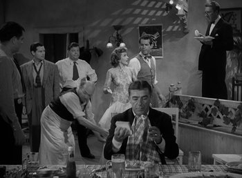 Movie still from “No Time for Love” (1943), directed by Mitchell Leisen – A group of people standing around a table; Wide shot, High angle