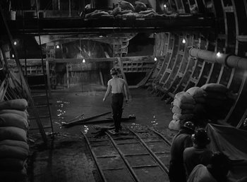 Movie still from “No Time for Love” (1943), directed by Mitchell Leisen – A man walking through a warehouse filled with bags of coal; Wide shot, High angle