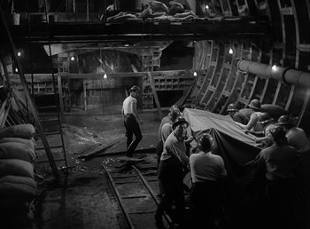 Movie still from “No Time for Love” (1943), directed by Mitchell Leisen – A group of men standing in a room next to a building; Wide shot, High angle