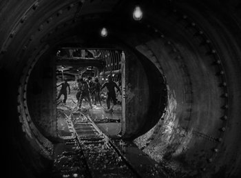 Movie still from “No Time for Love” (1943), directed by Mitchell Leisen – A black and white photo of a tunnel with a group of people walking through it; Extreme Wide shot, High angle