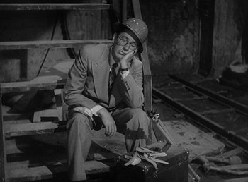 Movie still from “No Time for Love” (1943), directed by Mitchell Leisen – A man sitting on the ground in a suit and hat; Medium shot, High angle