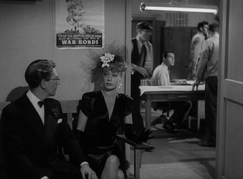 Movie still from “No Time for Love” (1943), directed by Mitchell Leisen – A man and a woman sitting next to each other in a room; Medium shot, Over the shoulder angle