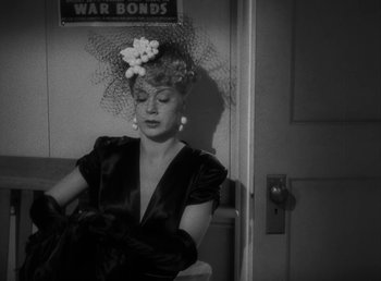 Movie still from “No Time for Love” (1943), directed by Mitchell Leisen – A black and white photo of a woman wearing a hat and gloves; Medium shot, Over the shoulder angle