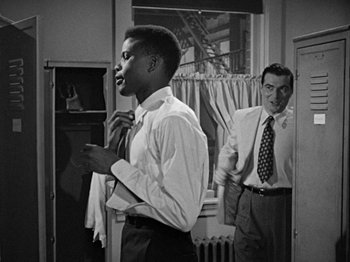 Movie still from “No Way Out” (1950), directed by Joseph L. Mankiewicz – A man in a suit and tie standing next to another man in a suit and tie; Medium shot, Over the shoulder angle