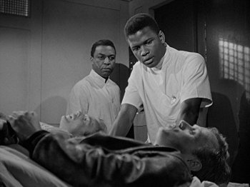 Movie still from “No Way Out” (1950), directed by Joseph L. Mankiewicz – A black and white photo of three men standing over a dead body; Medium shot, Over the shoulder angle