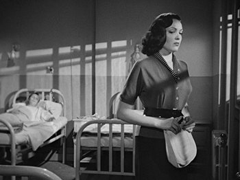Movie still from “No Way Out” (1950), directed by Joseph L. Mankiewicz – A woman standing in front of a chair in a room; Medium shot, Low angle
