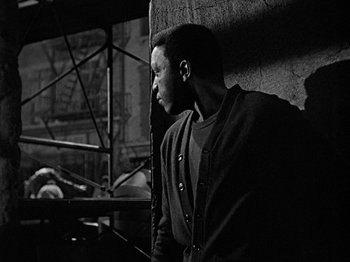 Movie still from “No Way Out” (1950), directed by Joseph L. Mankiewicz – A black and white photo of a man leaning up against a wall; Medium shot, Over the shoulder angle