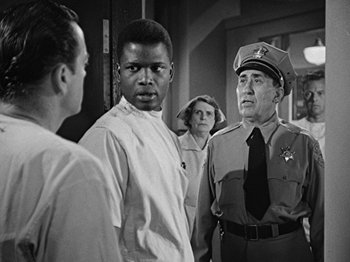 Movie still from “No Way Out” (1950), directed by Joseph L. Mankiewicz – A black and white photo of a man and two women; Medium shot, Over the shoulder angle