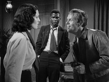 Movie still from “No Way Out” (1950), directed by Joseph L. Mankiewicz – A black and white photo of a man and a woman and a man with a gun; Medium shot, Over the shoulder angle