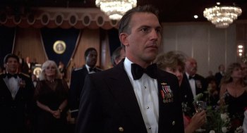 Movie still from “No Way Out” (1987), directed by Roger Donaldson – A man in a suit and bow tie standing in front of a crowd; Close Up shot, Low angle