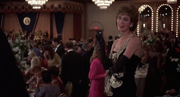 Movie still from “No Way Out” (1987), directed by Roger Donaldson – A woman in a black dress and black gloves at an event; Medium shot, Over the shoulder angle