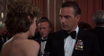 Movie still from “No Way Out” (1987), directed by Roger Donaldson – A man in a tuxedo is talking to a woman in a strapless dress; Close Up shot, Over the shoulder angle