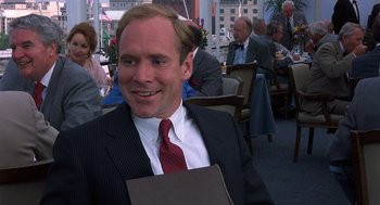 Movie still from “No Way Out” (1987), directed by Roger Donaldson – A man wearing a suit and tie holding a folder; Medium shot, Over the shoulder angle