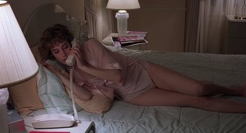 Movie still from “No Way Out” (1987), directed by Roger Donaldson – A woman laying on a bed talking on a phone; Medium shot, High angle