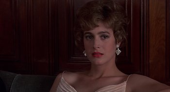 Movie still from “No Way Out” (1987), directed by Roger Donaldson – A woman in a white dress with earrings and red lipstick; Close Up shot, Low angle
