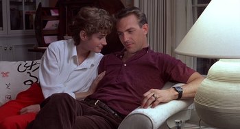 Movie still from “No Way Out” (1987), directed by Roger Donaldson – A man and a woman sitting on a couch together; Medium shot, Low angle