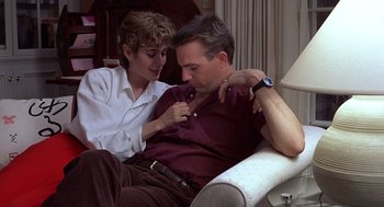 Movie still from “No Way Out” (1987), directed by Roger Donaldson – A man and a woman sitting on a couch together; Medium shot, Low angle