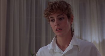 Movie still from “No Way Out” (1987), directed by Roger Donaldson – A young woman with curly brown hair wearing a white shirt; Close Up shot, Over the shoulder angle