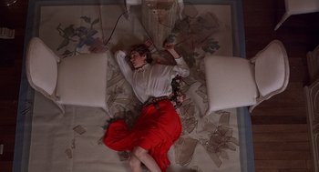 Movie still from “No Way Out” (1987), directed by Roger Donaldson – A woman is laying on the floor of a living room; Wide shot, Overhead angle