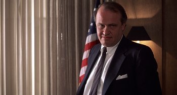 Movie still from “No Way Out” (1987), directed by Roger Donaldson – A man in a suit and tie standing in front of an american flag; Close Up shot, Low angle