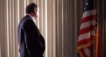 Movie still from “No Way Out” (1987), directed by Roger Donaldson – A man standing in front of an american flag in a room; Medium shot, Low angle