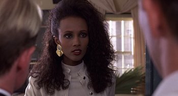 Movie still from “No Way Out” (1987), directed by Roger Donaldson – A woman with long curly hair wearing a white jacket; Close Up shot, Over the shoulder angle