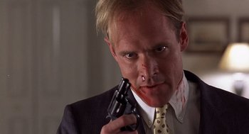 Movie still from “No Way Out” (1987), directed by Roger Donaldson – A person holding a gun with blood on his face; Close Up shot, Low angle