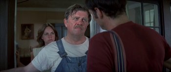 Movie still from “Norma Rae” (1979), directed by Martin Ritt – An older man in a white t - shirt and blue overalls talking to two other people; Close Up shot, Over the shoulder angle