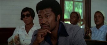 Movie still from “Norma Rae” (1979), directed by Martin Ritt – An older man with a beard and mustache is sitting in front of a group of people; Close Up shot, Low angle