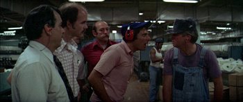 Movie still from “Norma Rae” (1979), directed by Martin Ritt – A group of men standing around in a room; Medium shot, Over the shoulder angle