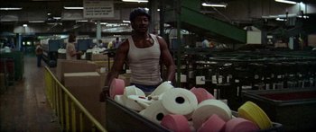 Movie still from “Norma Rae” (1979), directed by Martin Ritt – A man in white tank top pushing a cart of toilet paper; Medium shot, Low angle