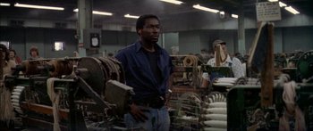 Movie still from “Norma Rae” (1979), directed by Martin Ritt – A man standing next to a machine in a factory; Medium shot, High angle