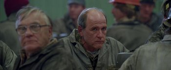 Movie still from “North Country” (2005), directed by Niki Caro – A man with a bald head is sitting in front of a group of people; Close Up shot, Over the shoulder angle