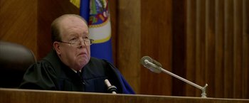 Movie still from “North Country” (2005), directed by Niki Caro – An old man in a judge's court room with a microphone; Close Up shot, Over the shoulder angle