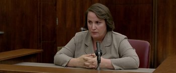 Movie still from “North Country” (2005), directed by Niki Caro – A woman sitting in front of a microphone in front of a wooden wall; Close Up shot, Over the shoulder angle