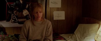 Movie still from “North Country” (2005), directed by Niki Caro – A woman sitting on a bed in front of a wooden wall; Medium shot, High angle