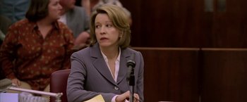 Movie still from “North Country” (2005), directed by Niki Caro – A woman in a gray suit sitting in front of a microphone in a courtroom; Close Up shot, Over the shoulder angle