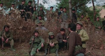 Movie still from “North Korean Partisan in South Korea” (1990), directed by Jeong Ji-yeong – A group of people in the woods sitting and standing around; Wide shot, High angle