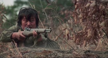 Movie still from “North Korean Partisan in South Korea” (1990), directed by Jeong Ji-yeong – A man is holding a rifle in the woods; Medium shot, Low angle