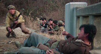 Movie still from “North Korean Partisan in South Korea” (1990), directed by Jeong Ji-yeong – A group of people sitting on the ground and looking at their cell phones; Medium shot, High angle