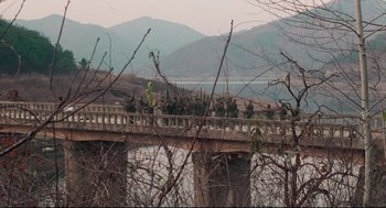 Movie still from “North Korean Partisan in South Korea” (1990), directed by Jeong Ji-yeong – A group of people walking across a wooden bridge; Extreme Wide shot, High angle