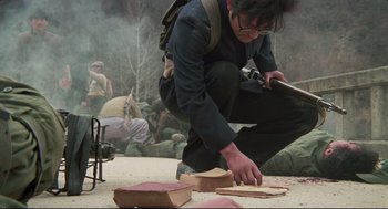Movie still from “North Korean Partisan in South Korea” (1990), directed by Jeong Ji-yeong – A man kneeling down on the ground with a book; Medium shot, High angle