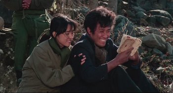 Movie still from “North Korean Partisan in South Korea” (1990), directed by Jeong Ji-yeong – A man and a woman sitting next to each other in the woods; Medium shot, High angle