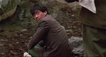 Movie still from “North Korean Partisan in South Korea” (1990), directed by Jeong Ji-yeong – A man sitting on the ground near a body of water; Medium shot, High angle