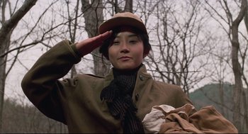 Movie still from “North Korean Partisan in South Korea” (1990), directed by Jeong Ji-yeong – A woman saluting in front of a tree; Close Up shot, Low angle