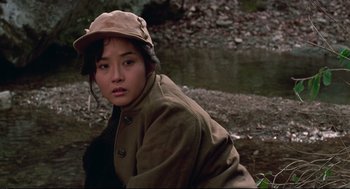 Movie still from “North Korean Partisan in South Korea” (1990), directed by Jeong Ji-yeong – A woman in a hat and a coat is by a river; Close Up shot, Over the shoulder angle