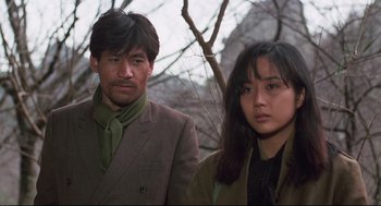 Movie still from “North Korean Partisan in South Korea” (1990), directed by Jeong Ji-yeong – A man and a woman standing next to each other in front of trees; Close Up shot, Low angle