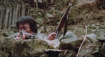 Movie still from “North Korean Partisan in South Korea” (1990), directed by Jeong Ji-yeong – A man laying on the ground holding a rifle; Medium shot, High angle