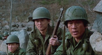 Movie still from “North Korean Partisan in South Korea” (1990), directed by Jeong Ji-yeong – Two men in green uniforms and helmets are holding a rifle; Close Up shot, Low angle