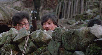 Movie still from “North Korean Partisan in South Korea” (1990), directed by Jeong Ji-yeong – A man holding a rifle while standing next to a wall; Medium shot, Low angle